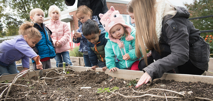 Young children working in campus garden with a student