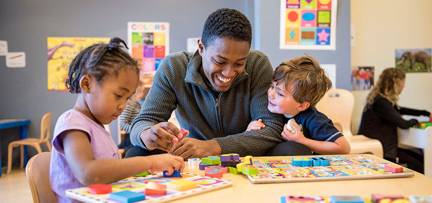 A SUNY Cortland student helps two children with wooden puzzles in the Child Care Center