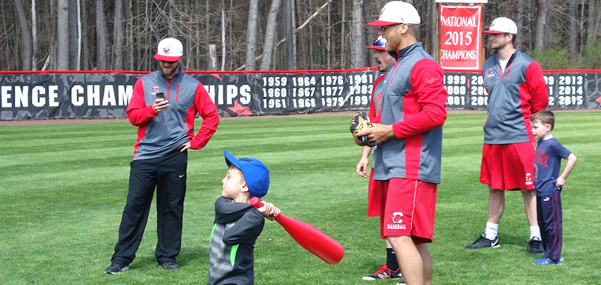 Local child swinging a bat with Cortland baseball players looking on
