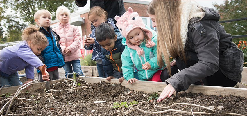 Cortland students help preschool students plant flowers in a raised bed