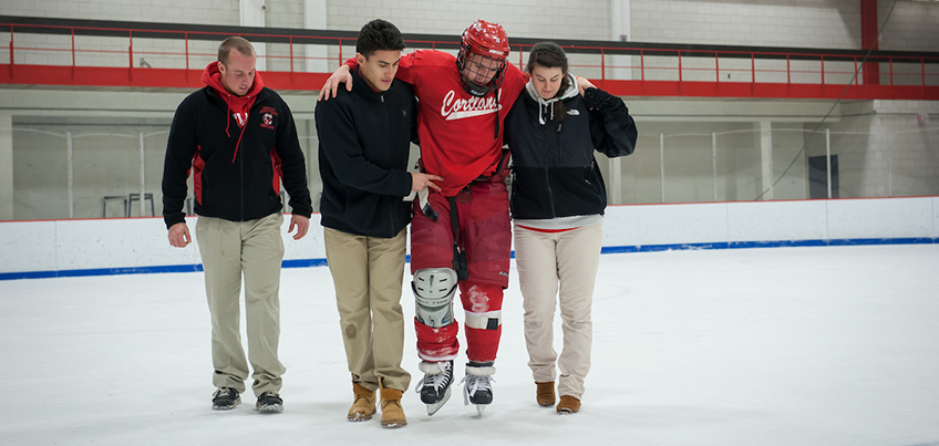 Athletic training students help carry a hockey player off the ice