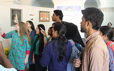 classmates in India browse paintings created by SUNY Cortland students