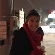 Beth standing in snow, holding a coffee and smiling at the camera