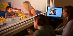 A student works with a child in the Communication Disorders lab while other students observe