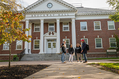 Five students standing in a semi-circle, talking outside the front entrance of Brockway Hall