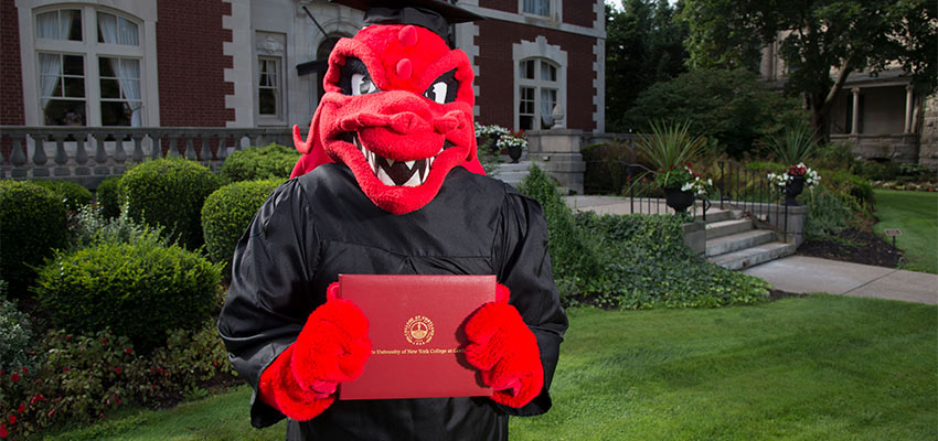 Blaze holding a diploma in front of the Lynne Parks '68 Alumni House