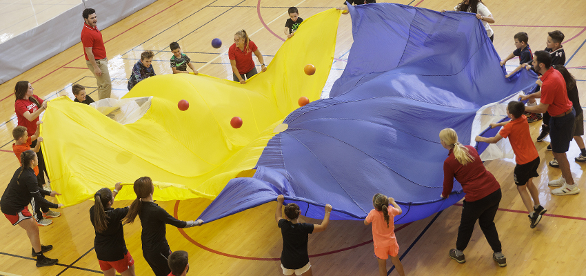 Physical education students lead schoolchildren in a large parachute activity