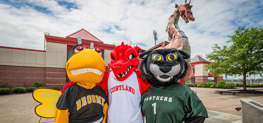 The Broome and Tompkins Community College mascots standing next to SUNY Cortland's Blaze mascot outside of the football stadium