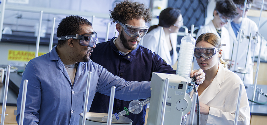 Two students working in a chemistry lab as a faculty member instructs them