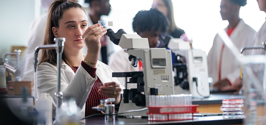 Biology major holds up slide next to microscope