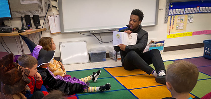 Student reads to kindergartners in costumes at a local school