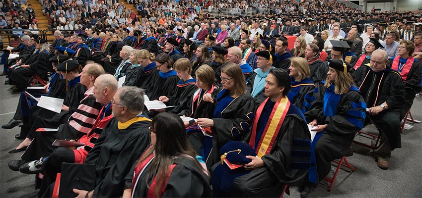 Faculty and staff in regalia sit at a commencement ceremony
