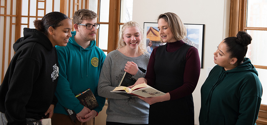 Graduate students in English look on as a faculty member reads from a textbook