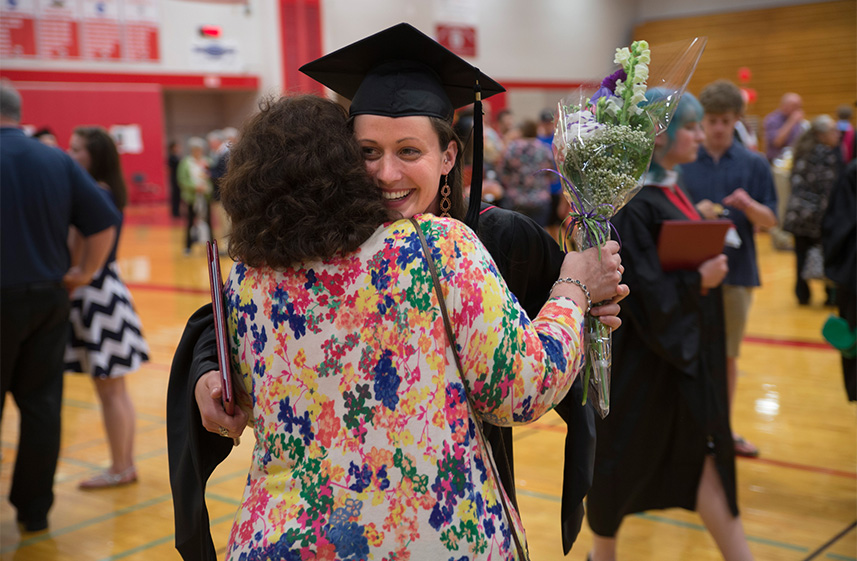 Student and faculty member hug at Graduate Commencement