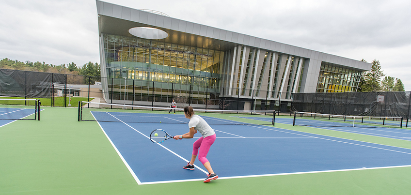 Person plays tennis on the courts outside of the Student Life Center
