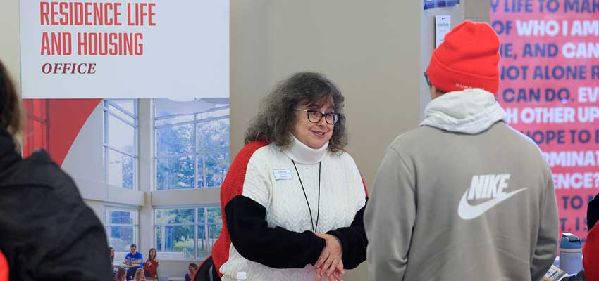 Staff Member talking to a student with the Residence Life and Housing banner behind them.