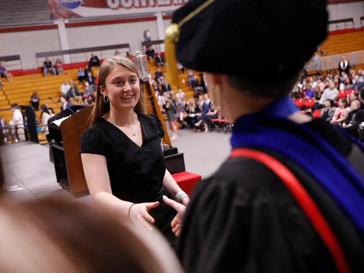 Student at Honors Convocation shakes the hand of a professor in regalia