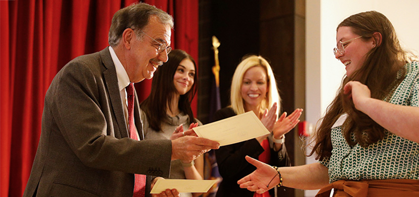 President Erik J. Bitterbaum hands an award certificate to a smiling student at a President's List awards ceremony