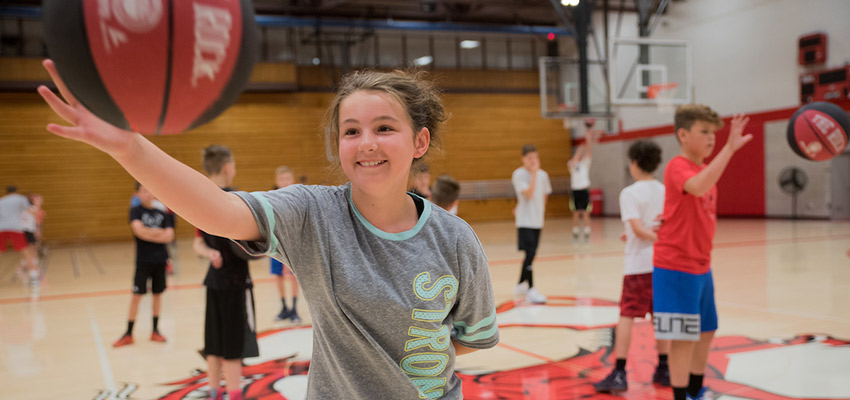 Girl catching a basketball while practicing in the gym at a summer sports camp