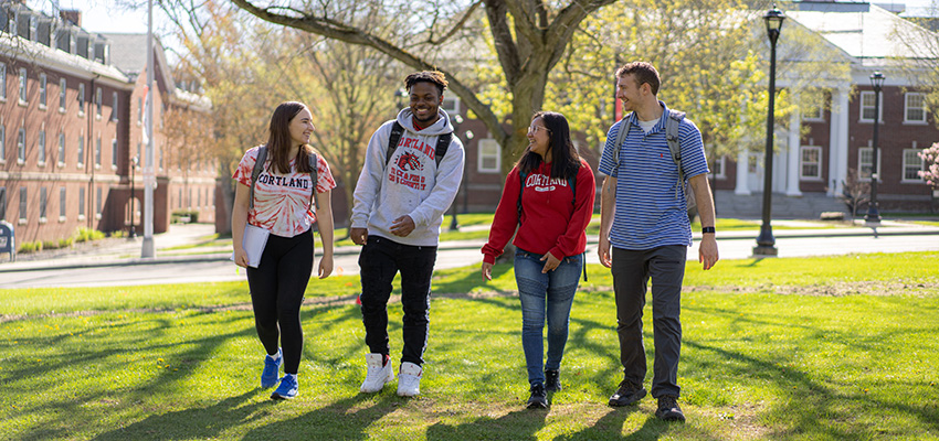 Four students walking in a group outside with Brockway Hall in the background