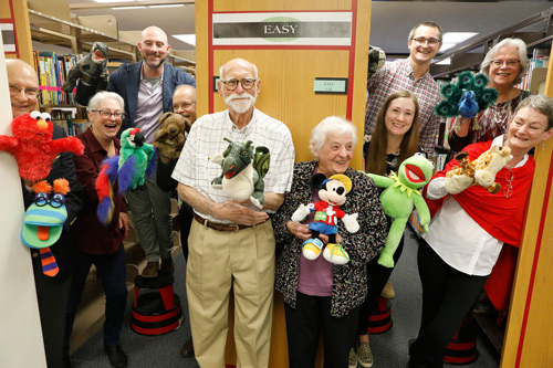 The Fralick family posing with puppets in front of bookshelves