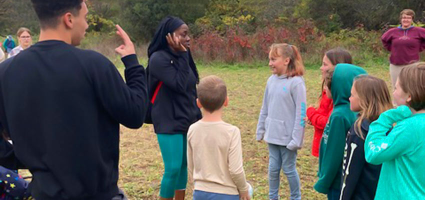 SUNY Cortland professor, Tracy Hudson, and PE student playing with children of the Forest Learning Collective