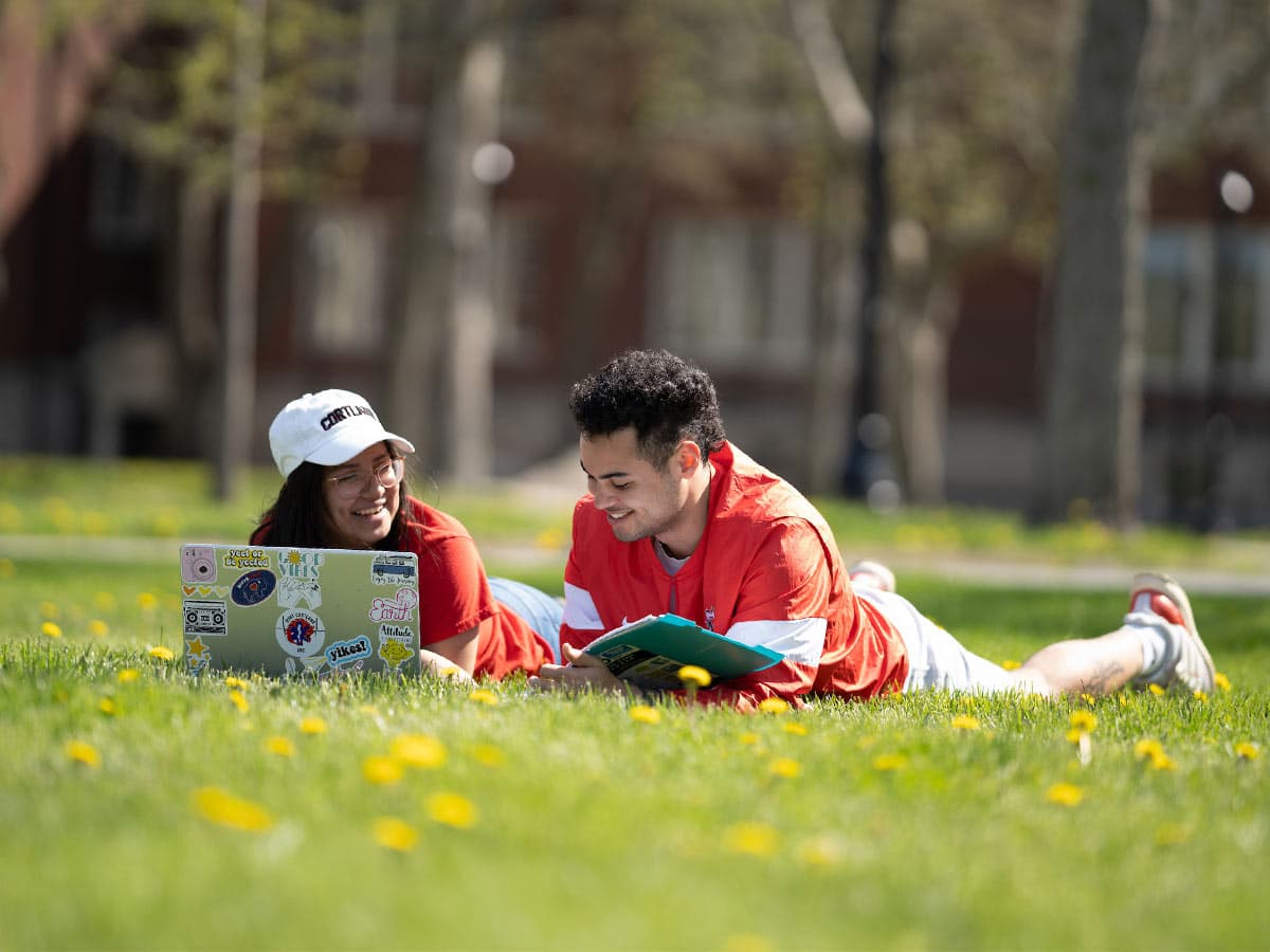 Students with a laptop lying on a lawn in the sun