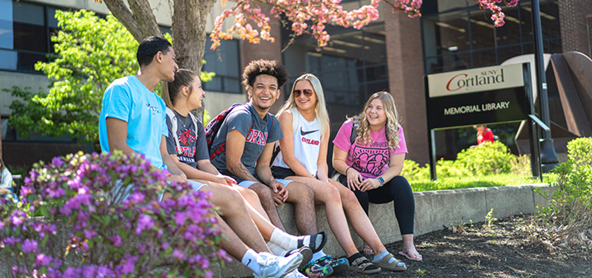 Students sitting outside Memorial Library and laughing under a tree