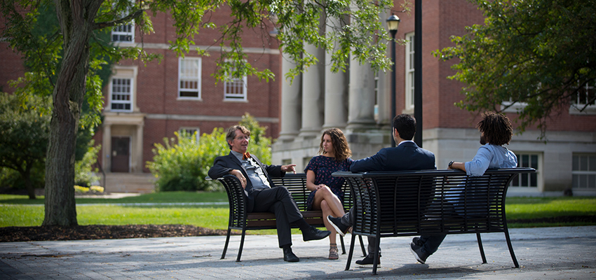 A group of four campus community members share a conversation on the benches outside Old Main