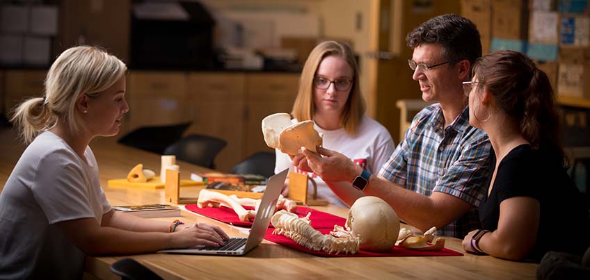 Students and professor in lab examining a skeleton