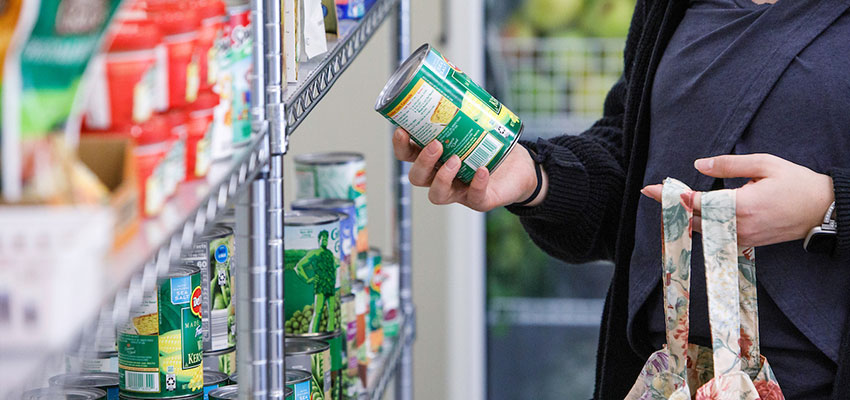 Woman picking up a can of corn from a shelf in the Cortland Cupboard