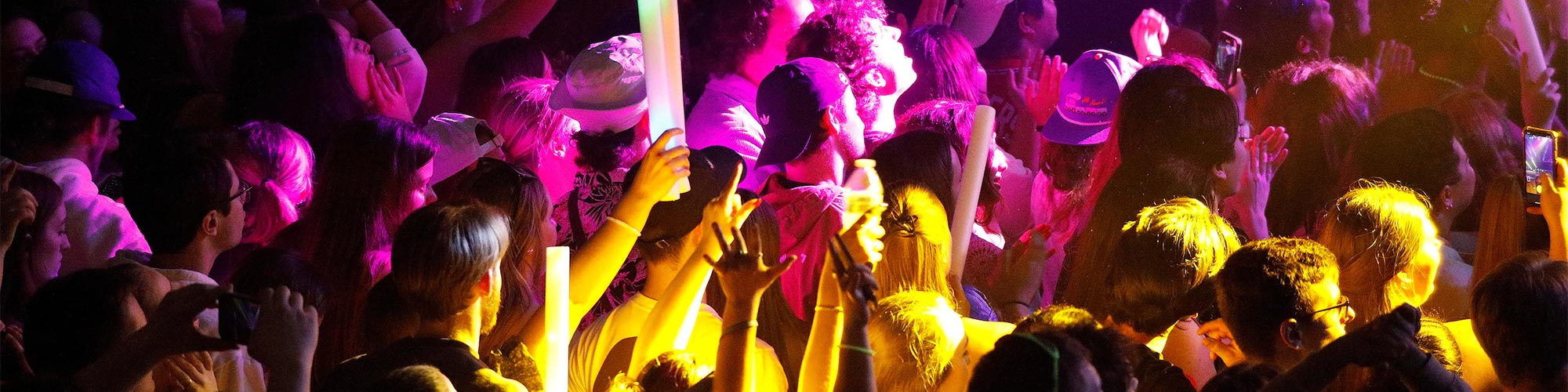 Pink and yellow lights shine on a crowd of concert goers