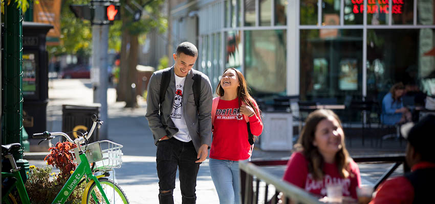 Two students laughing and walking together in downtown Cortland near Bru 64 and Brix