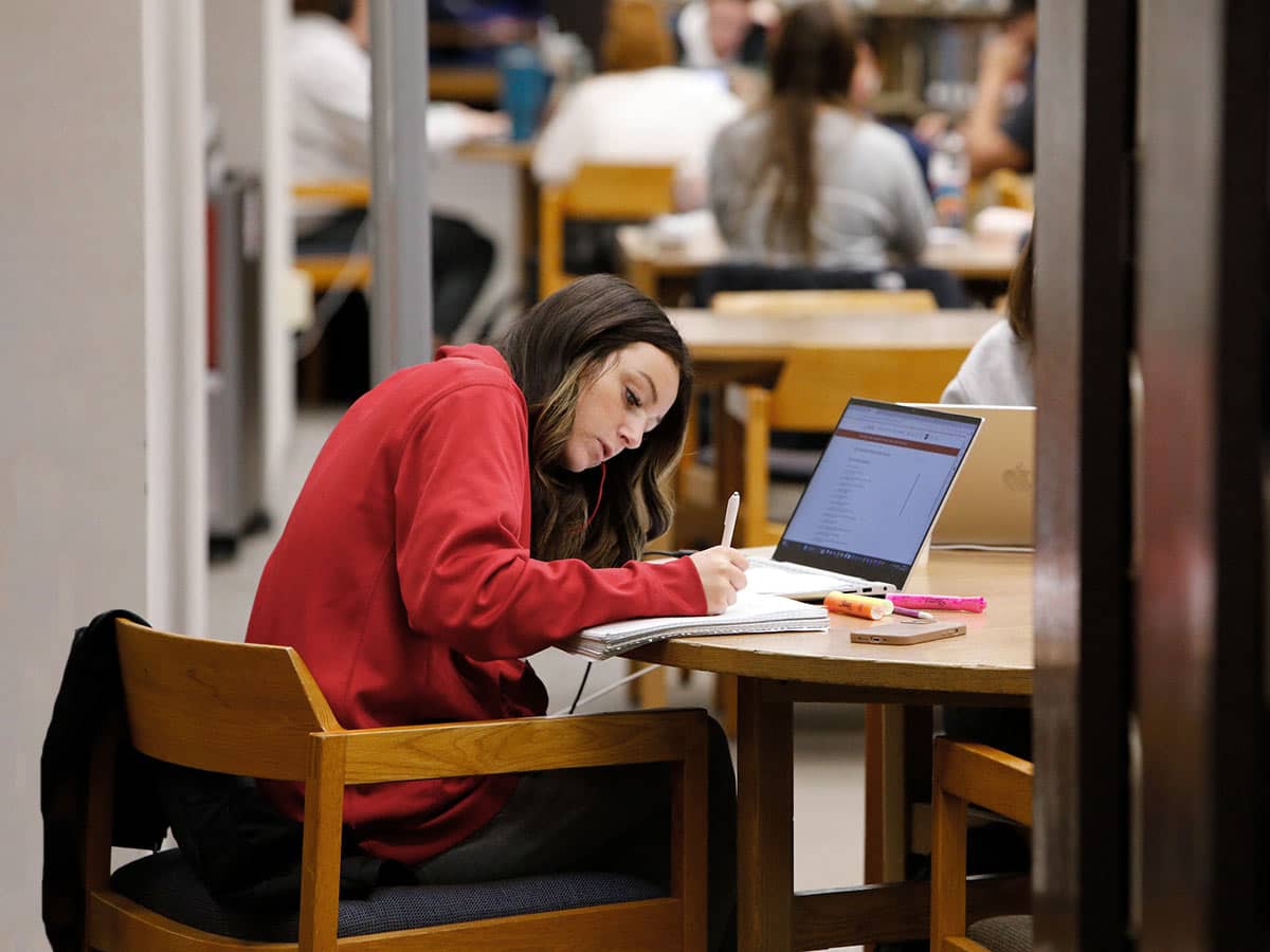 Student writing in notebook with laptop open in the Memorial Library