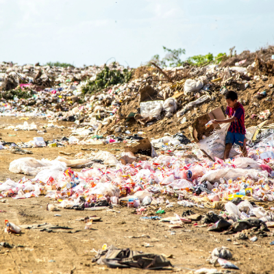 A child collecting plastic waste in a large landfill under a bright sky, photo taken by Hermes Rivera