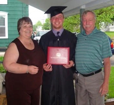 College graduate Casey O'Keefe is pictured in a black robe holding up his diploma cover in between his parents at his Cortland graduation.