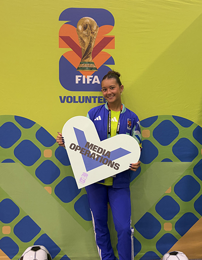 Julia Kito stands in front of a yellow FIFA World Cup background display