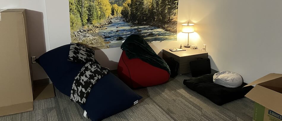 A view of the sensory room showing various floor pillows for meditation and relaxation, a floor table with a lamp, and a nature tapestry on the wall