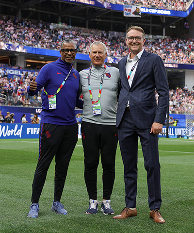 Three soccer staff members stand on a soccer field at the FIFA World Cup