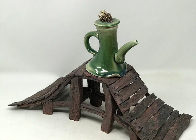 A sculpture of a whimsical green teapot on top of a small bridge