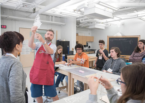 An instructor holding up a lacy piece of paper in front of a group of students