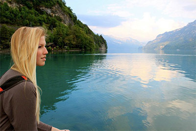 Study Abroad Page Link - Study Abroad participant looking off onto green mountains and calm lake