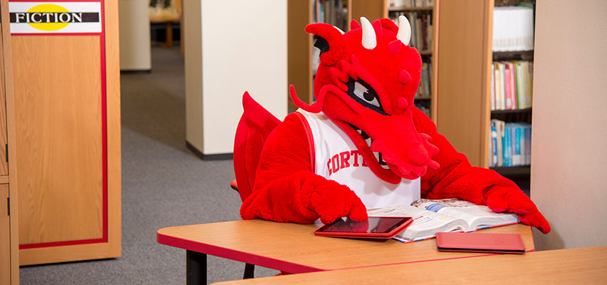 Blaze studies from a textbook while using a tablet, sitting in the Teaching Materials Center