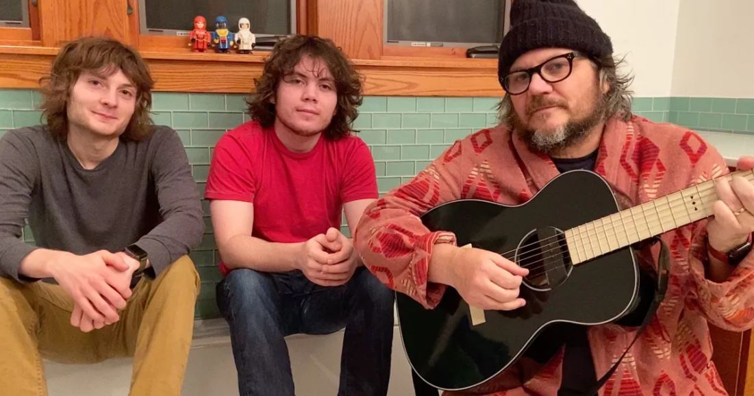 Jeff Tweedy holding a guitar, seated with his sons