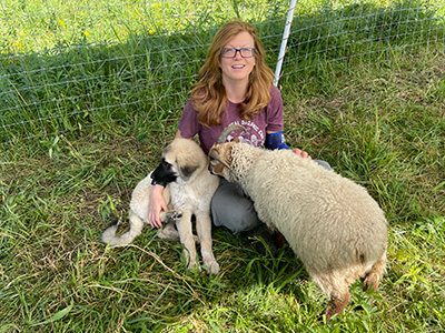Dr. Jena Nicols Curtis smiling with her dog and sheep