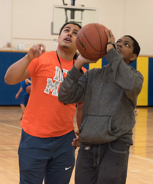 Physical education teacher on left instructs a middle school boy shooting a basketball