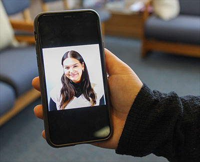 A hand holding a phone, with a professional headshot photo displaying