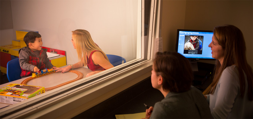 A student working with a child in a speech clinic, while a student a professor observe