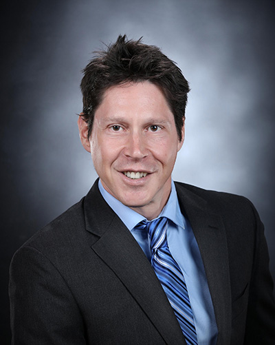 Portrait of Christopher Badurek in a suit and gray background