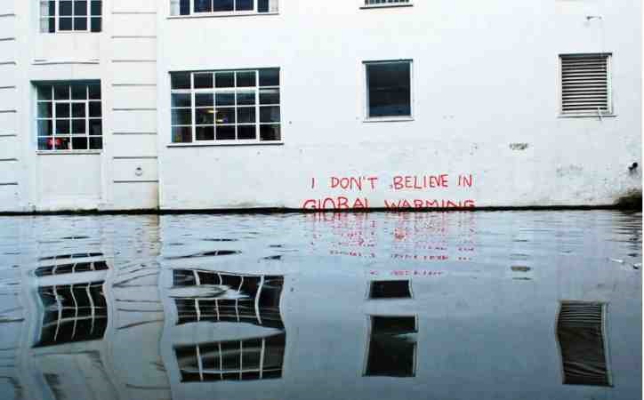 building with "I don't believe in global warming" graffiti partially obscured by rising flood waters